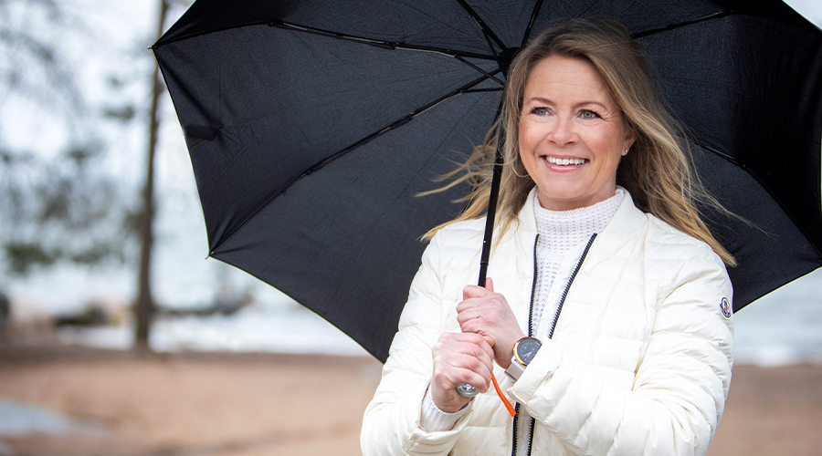 Kuntarahoituksen leasing-asiantuntija Krista Peltomäki. Vaaleahiuksinen, hymyilevä nainen valkoisessa kevyttoppatakissa kantaa mustaa sateenvarjoa.