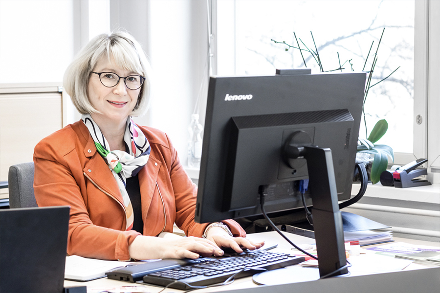 Mielen ry:n toiminnanjohtaja Maarit Hirvonen istuu tietokoneen ääressä valoisassa toimistohuoneessa ja katsoo kameraan.