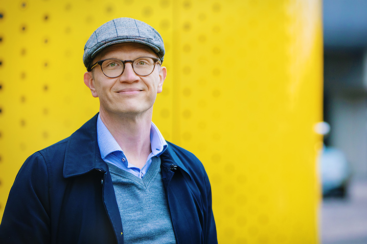 Kuntarahoituksen pääekonomisti Timo Vesala kuvattuna lakki päässä keltaista seinää vasten.