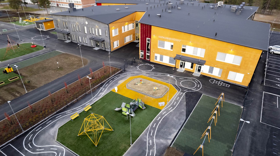 Ilmakuva: Tähtikunnan koulu Sodankylässä. Kelta- ja harmaaseinäinen, epäsäännöllisen muotoinen, kaksikerroksinen rakennus. Etualalla piha, jossa ulkoleikkivälineitä.
