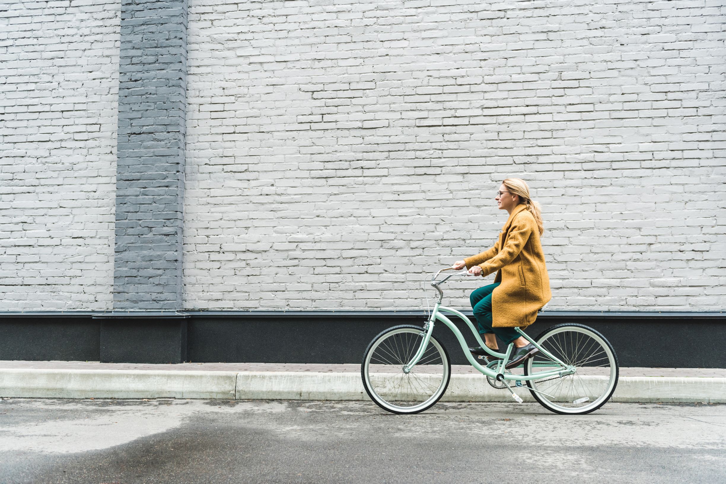 A woman in yellow coat riding bicycle with grey wall on background.