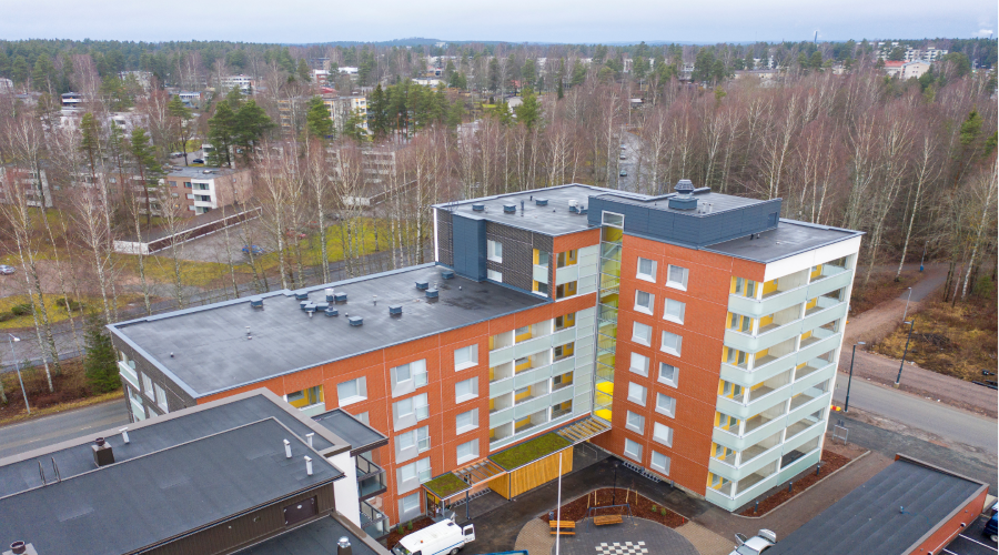 Kuvassa on L:n muotinen kerrostalo, jonka värityksessä on oranssia ja valkoista.