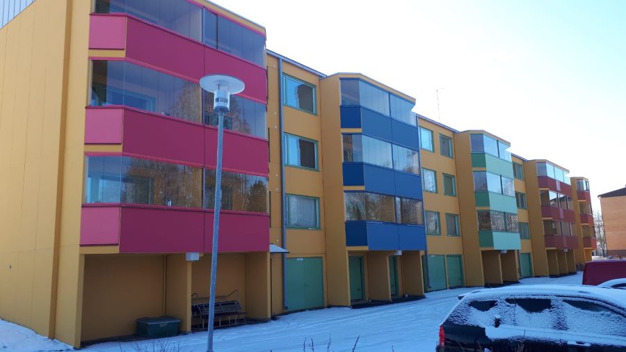 Kuvassa on kerostalo, jonka neljä rappua ovat eri värisiä ja joissa on isot parvekkeet.