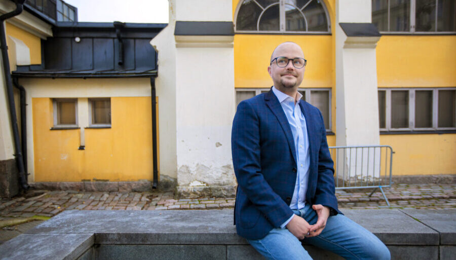 Kuvassa Inspiran Olli Immonen istuu ulkona värikkään rakennuksen edessä.