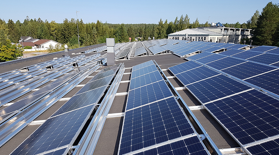 Aurinkopaneleeja rakennuksen katolla Vihdissä. Taustalla metsää ja taivasta.