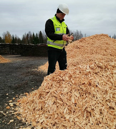 Huomioliiveihin ja kypärään pukeutunut Mikko Mursula seisoo puuhakekasan vieressä ja tutkii haketta.