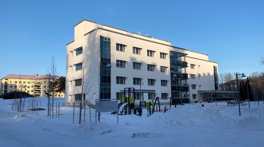 Kuvassa on valkoinen nelikerroksinen kerrostalo talvimaisemassa.