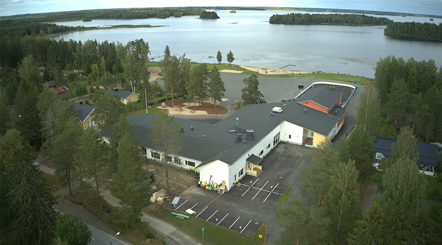 Kuvassa on koulu ja päiväkoti kauniissa maisemassa järven rannalla.