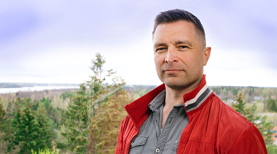 Jani Kervinen lähikuvassa, taustalla rakennusten kattoja, puita ja taivasta.