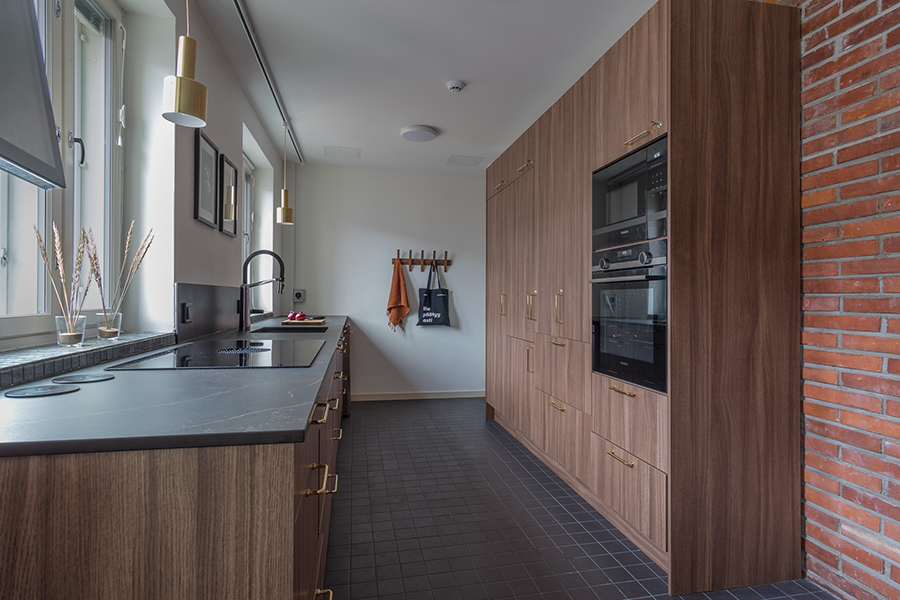A view of Satakuntatalo’s modern kitchen, with small cabinets and a sink on the window wall, and large cabinets and kitchen appliances on the opposite wall.