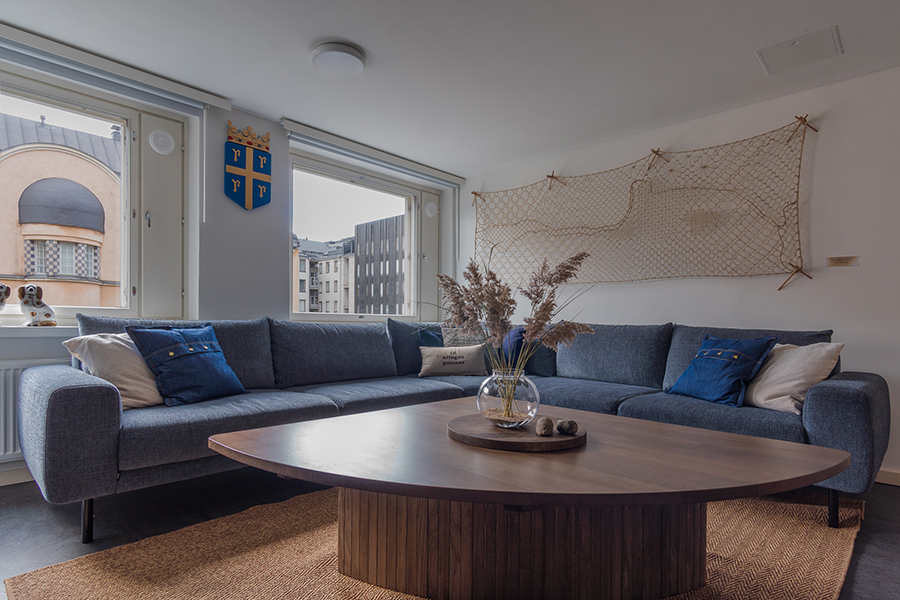 Common area with a large blue corner sofa and a wooden coffee table. A window at the back and a fishing net on the other wall.