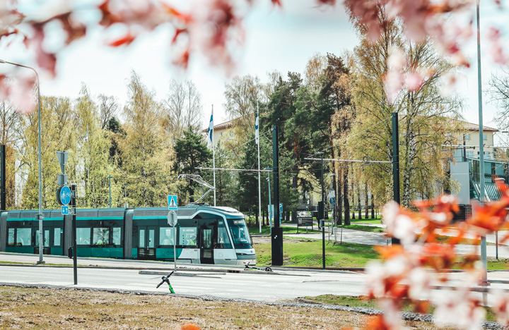 Kuvassa raitovaunu liikenteesä. taustalla on puistoalue.