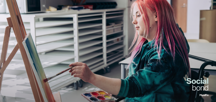 A person with long ping hair seating and painting a picture in a building financed with MuniFin social bonds.