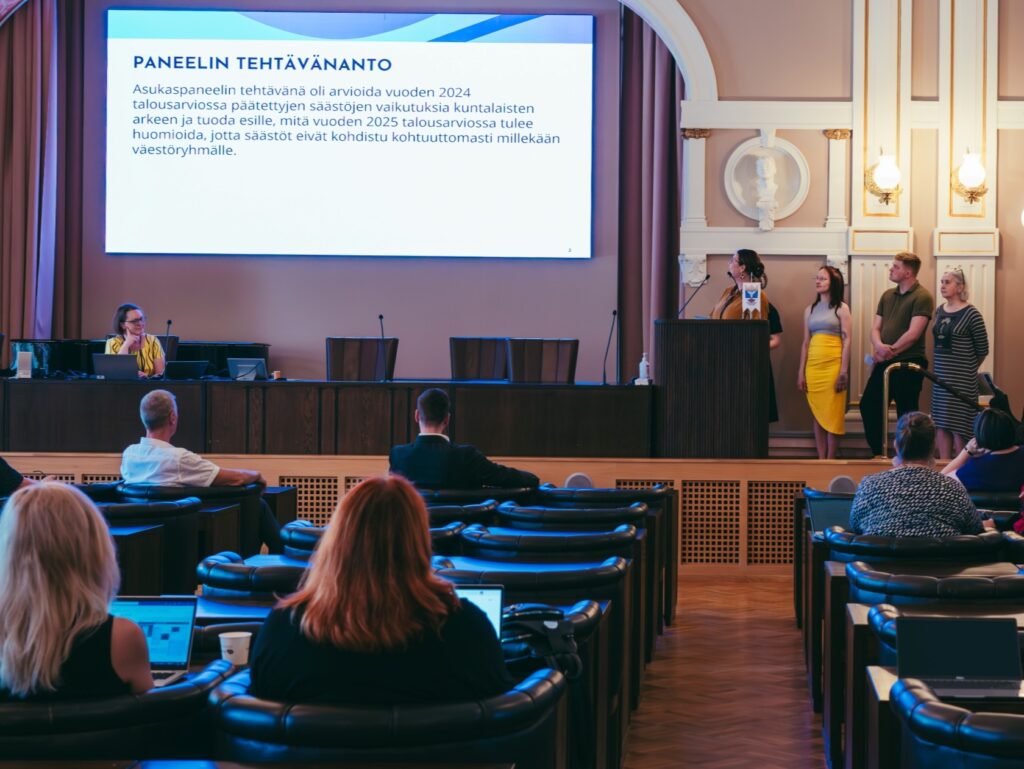 Ihmisiä istumassa salissa valmistautumassa paneelikeskusteluun